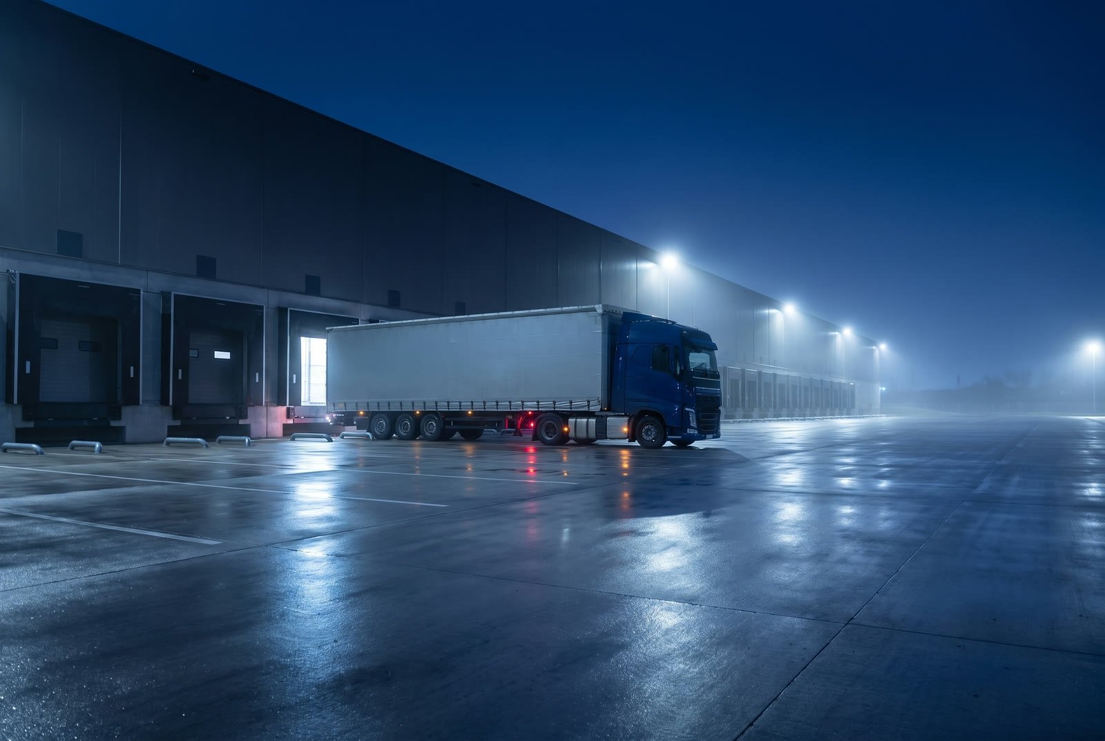 Un bilico con cabina blu fermo alle ribalte di un hub logistico, di notte